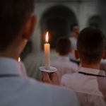 Boys in a church choir hold candles during a rehearsal, creating a warm and religious atmosphere.