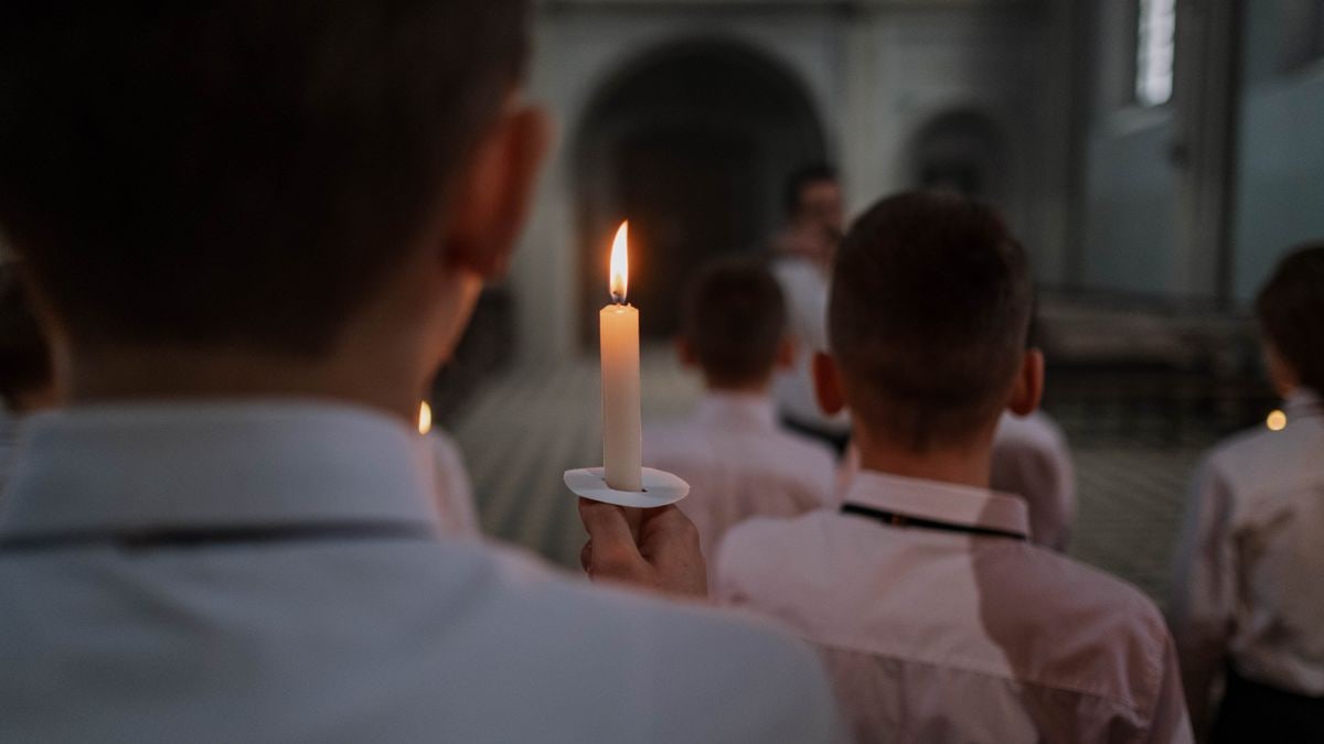 Boys in a church choir hold candles during a rehearsal, creating a warm and religious atmosphere.
